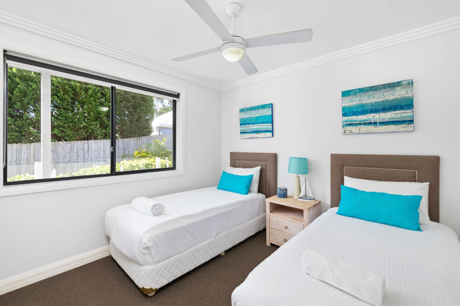 Un dormitorio luminoso con dos camas, ropa de cama blanca y cojines azules.