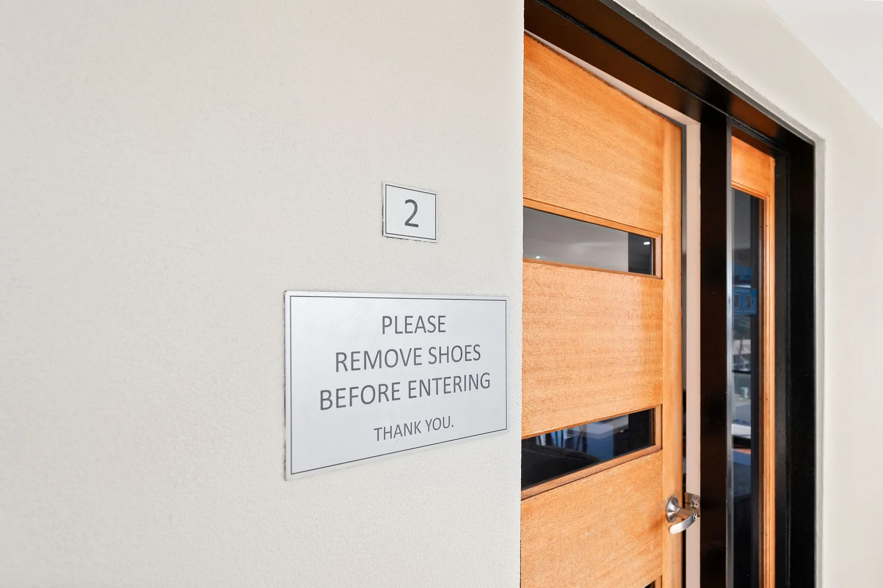 Una entrada con una puerta de madera y un cartel que pide quitarse los zapatos.