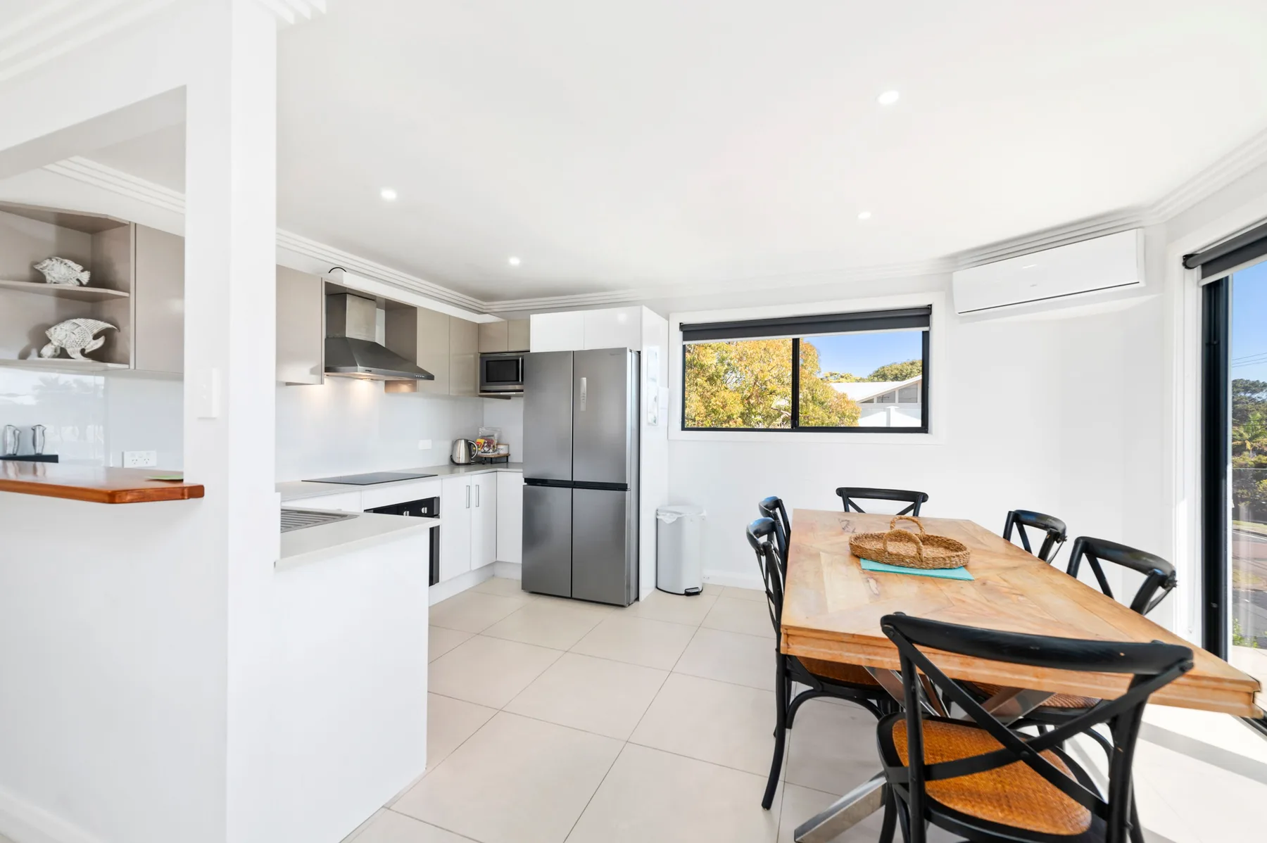 A bright kitchen and dining area with a wooden table and black seating.