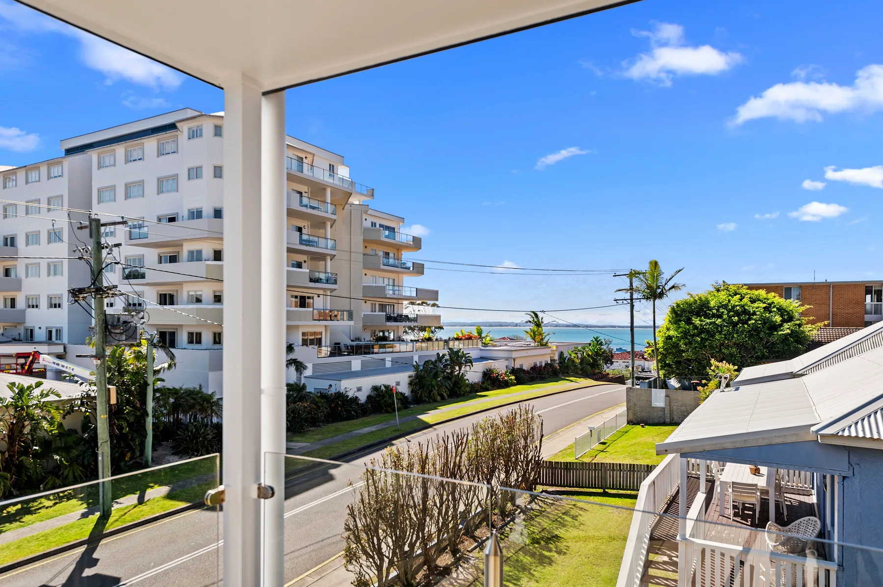 A balcony overlooks a street, nearby buildings, and a glimpse of water.