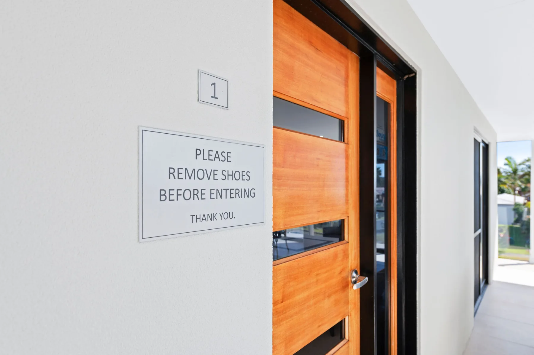 Una entrada exterior con una puerta de madera y un letrero que pide quitarse los zapatos.