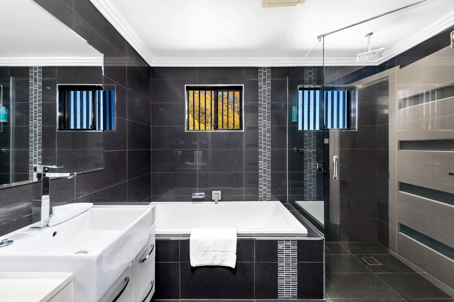 Un baño de azulejos oscuros con bañera, lavabo y ducha de vidrio.