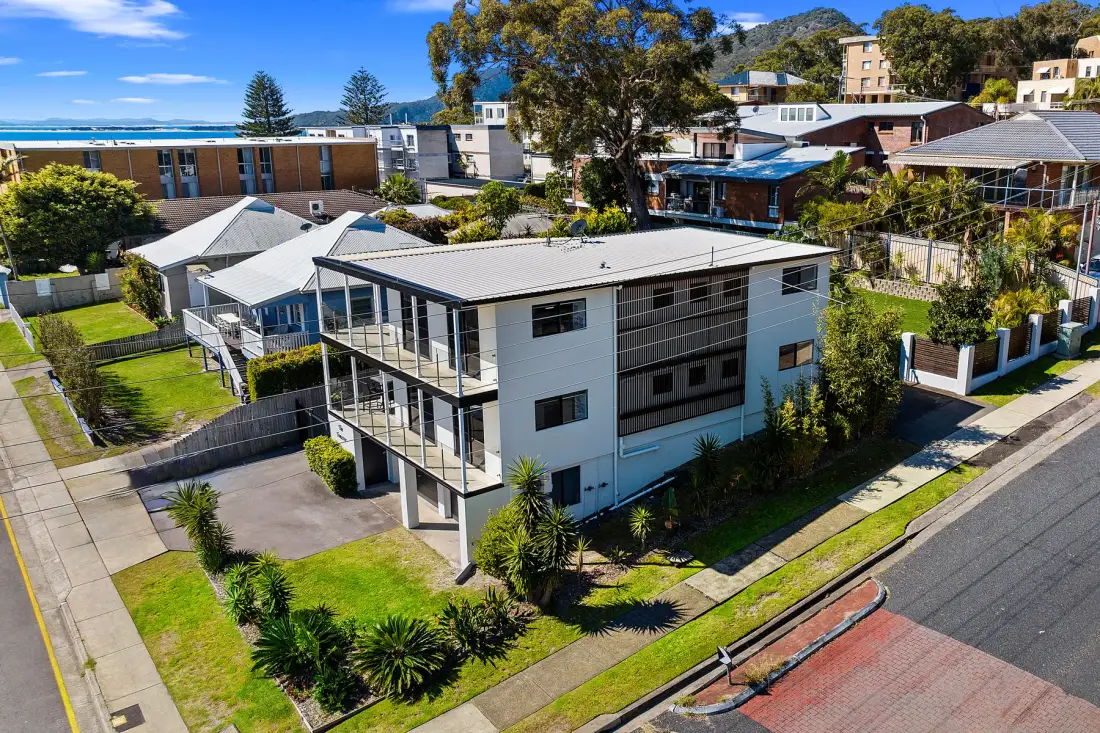 Vista aérea de un edificio moderno entre casas y árboles cerca de la costa.