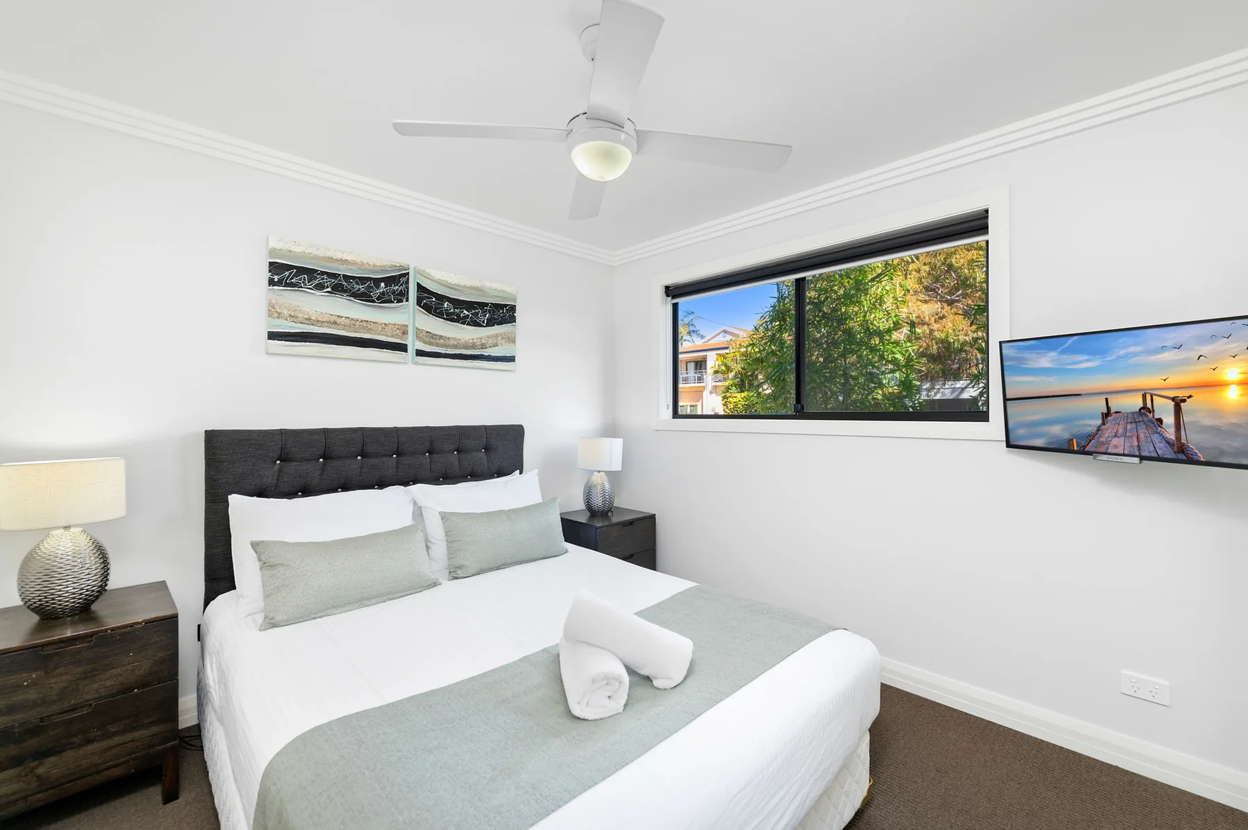 Un dormitorio luminoso con una cama arreglada y una ventana con vistas a los árboles.