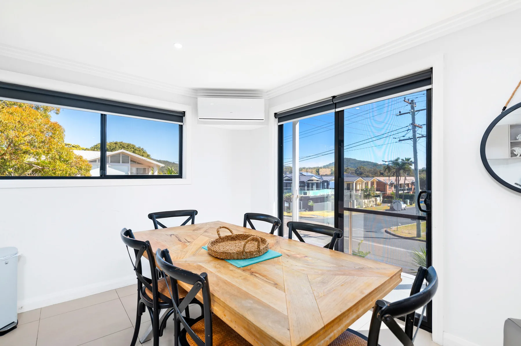 Un comedor luminoso con una mesa de madera y asientos negros junto a grandes ventanas.