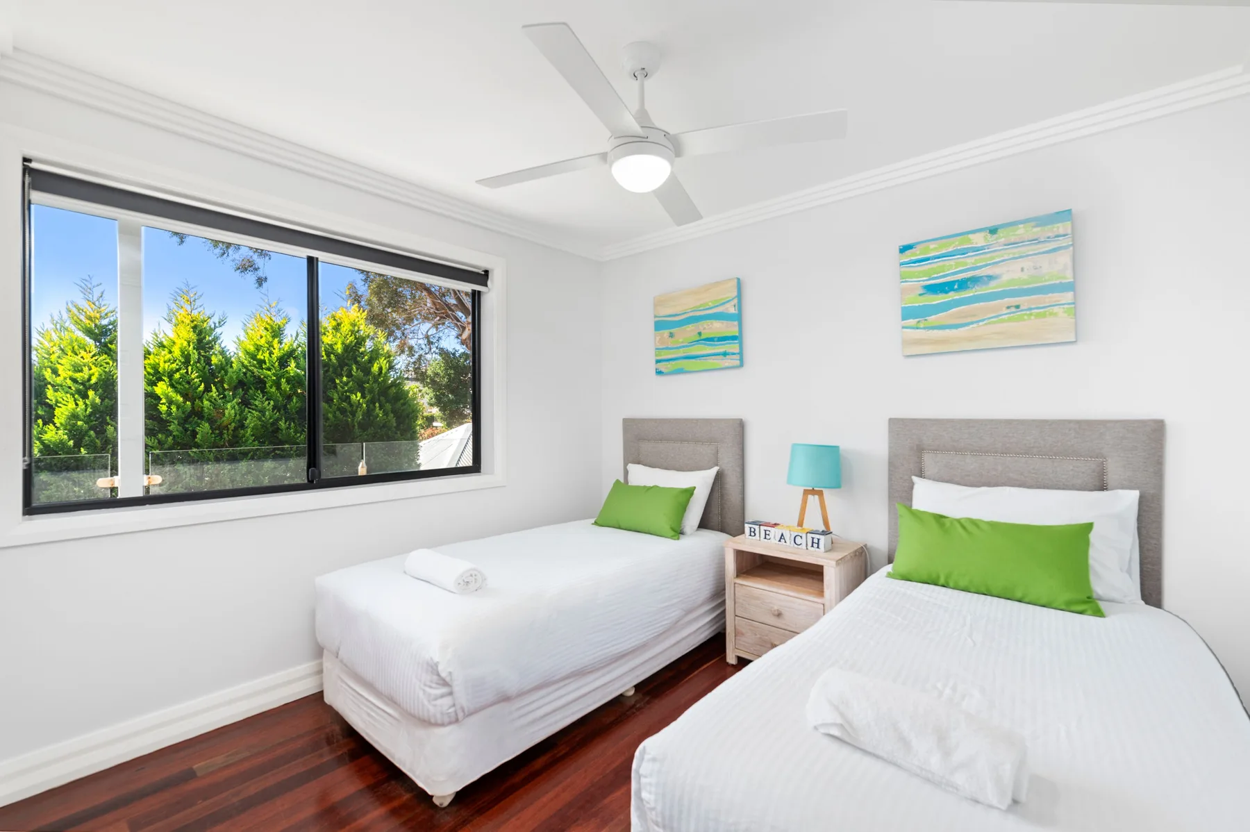 Un dormitorio luminoso con dos camas, cojines verdes y una ventana amplia.