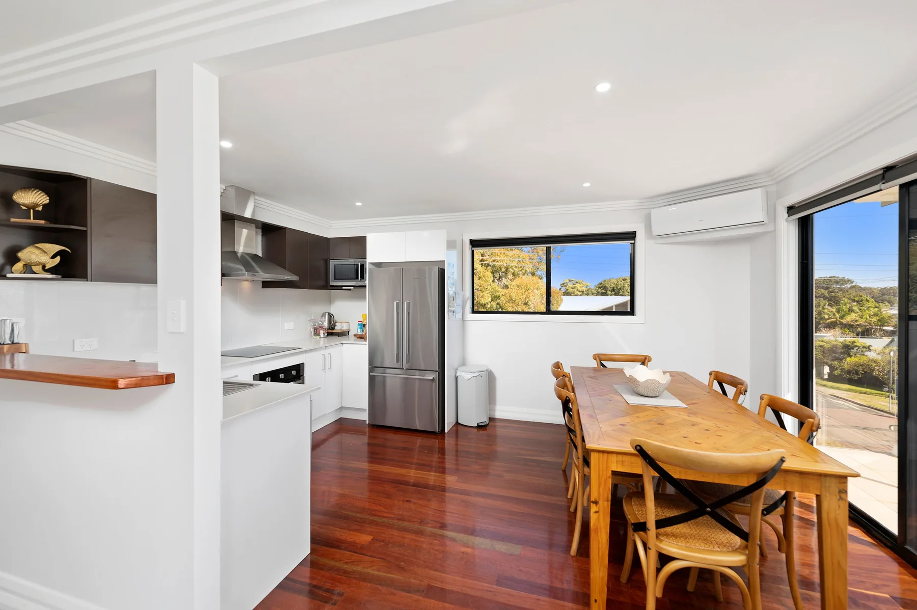Una cocina luminosa con comedor y una mesa de madera junto a grandes ventanas.