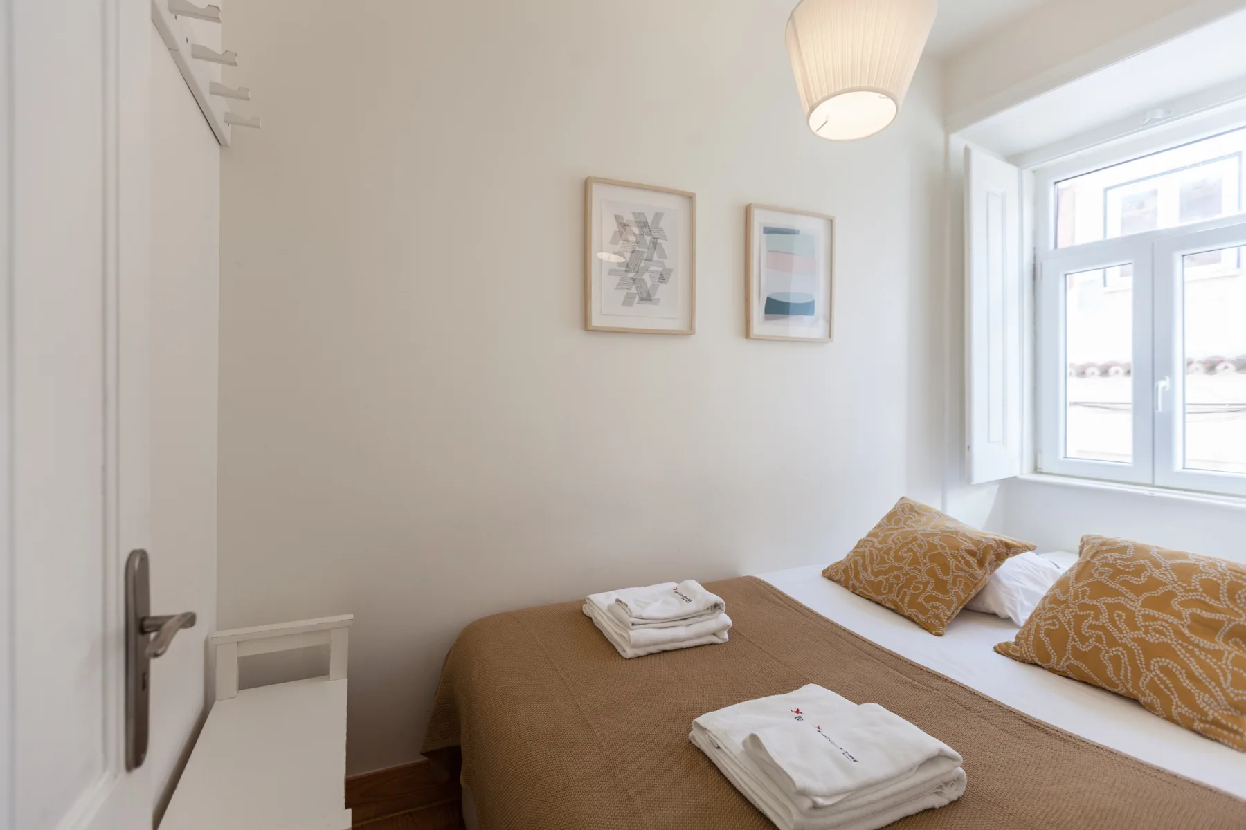 A bright bedroom with a double bed, patterned pillows, and a large window.