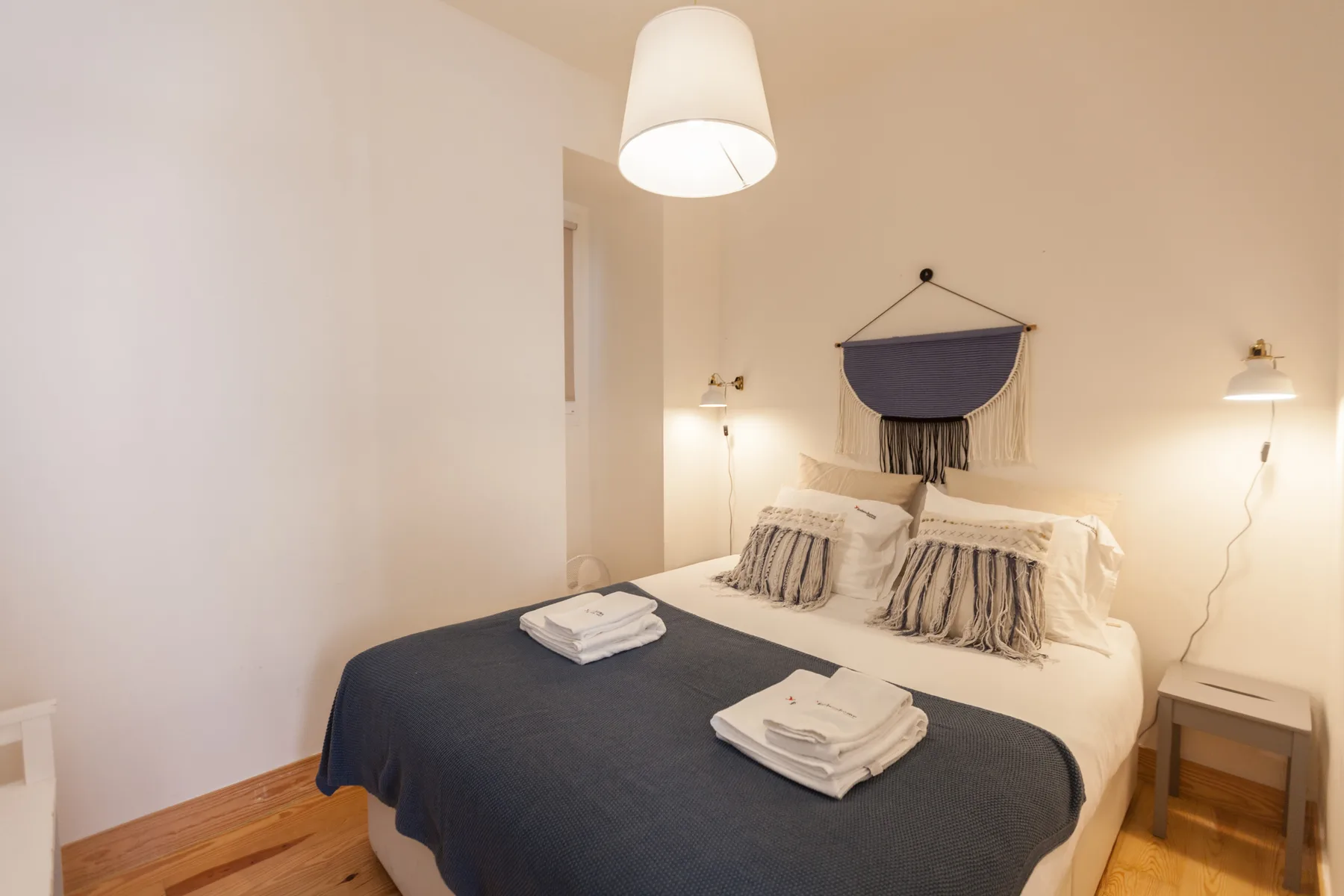 A bedroom with a bed, folded towels, and wall-mounted bedside lights.
