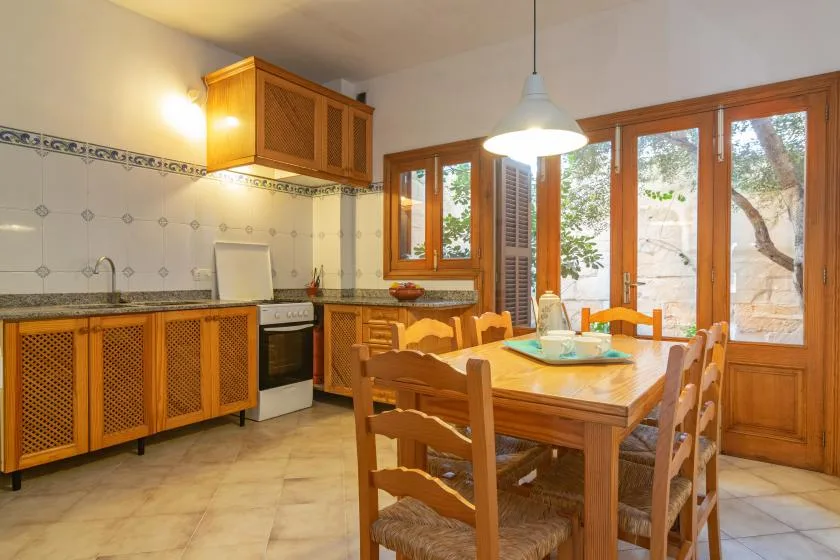Una cocina y comedor con armarios de madera, una mesa y ventanas grandes.