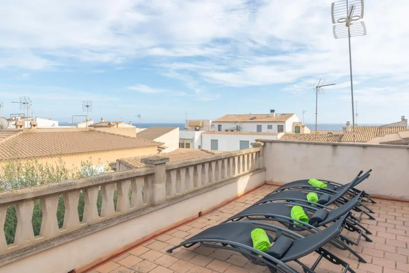 Una terraza en la azotea con tumbonas ofrece vistas de edificios cercanos y del mar.