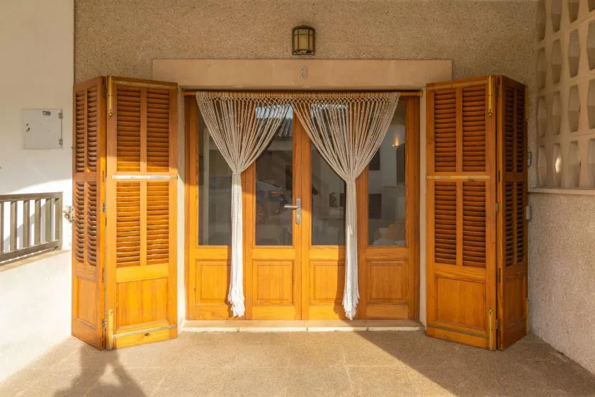Puertas de madera con cortinas transparentes se abren a una terraza soleada.