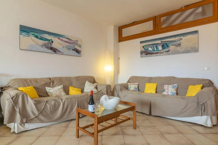 Una sala de estar con asientos, cojines coloridos y cuadros de temática playera.