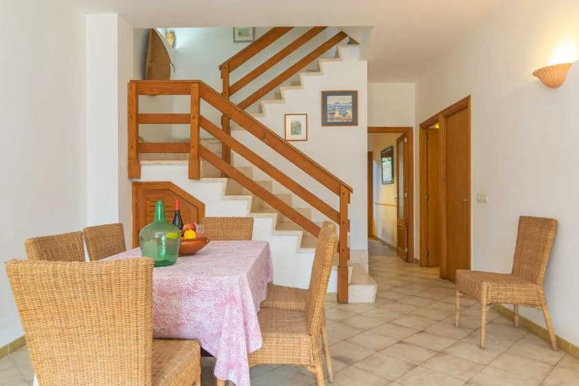 Comedor con una mesa y asientos de mimbre bajo una escalera de madera.