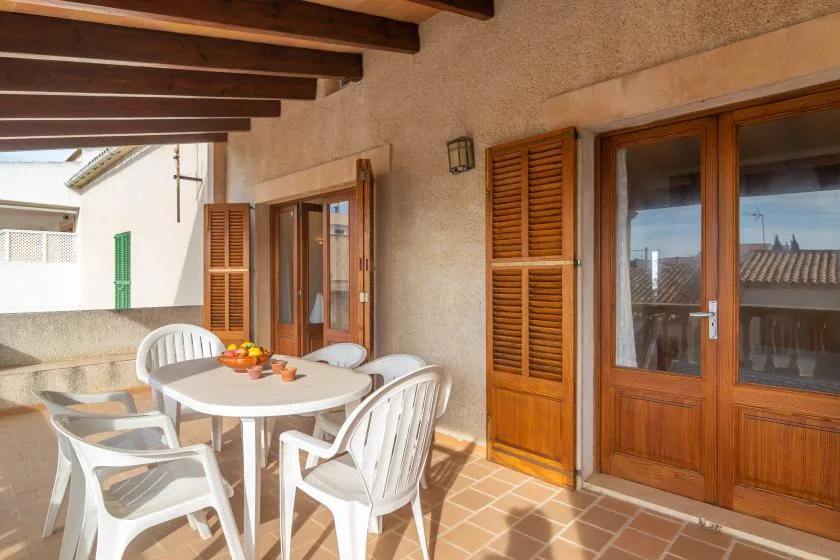A covered patio with a round table and white seating beside wooden doors.