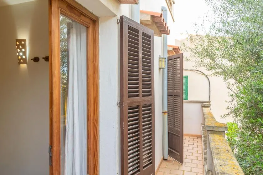 Un estrecho pasillo exterior bordea un edificio con contraventanas de madera y una puerta de vidrio.