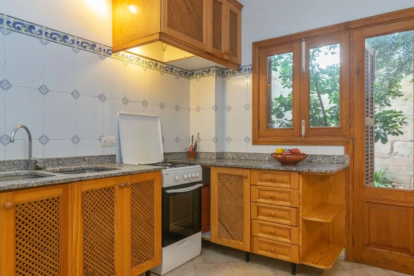 Una cocina alicatada con armarios de madera, una estufa y ventanas con vistas a la vegetación.