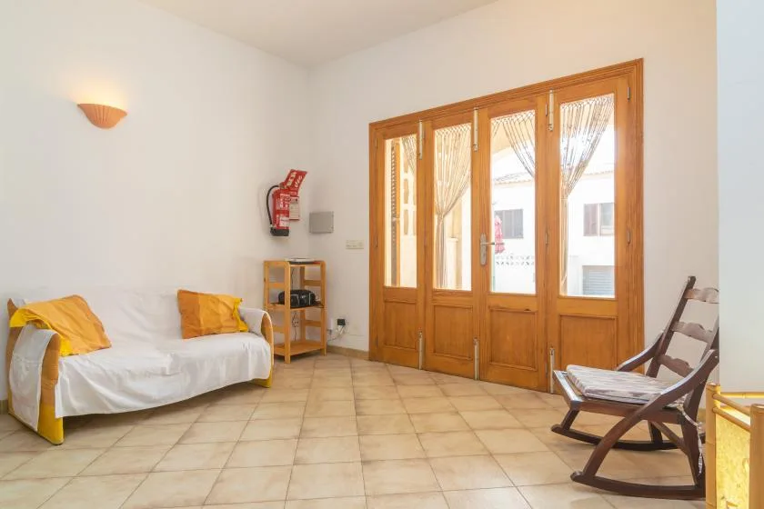 Una sala de estar luminosa con asientos y altas puertas de madera que dan a un balcón.