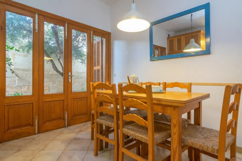 Una mesa de comedor de madera y sillas están junto a puertas altas de vidrio, con un espejo de marco azul en la pared.