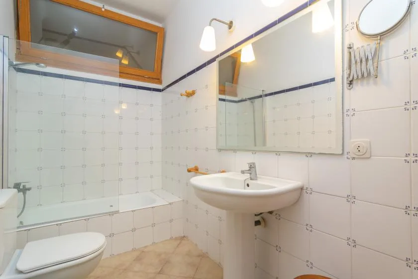 Un baño alicatado con ducha de vidrio, espejo de pared y lavabo blanco.
