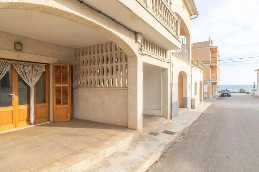 Una calle junto a una hilera de edificios, con una entrada retranqueada y el mar visible a lo lejos.
