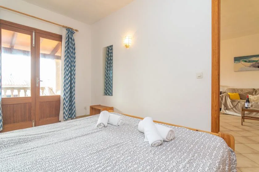 Un dormitorio con una colcha estampada, toallas y puertas de cristal que dan a un balcón.