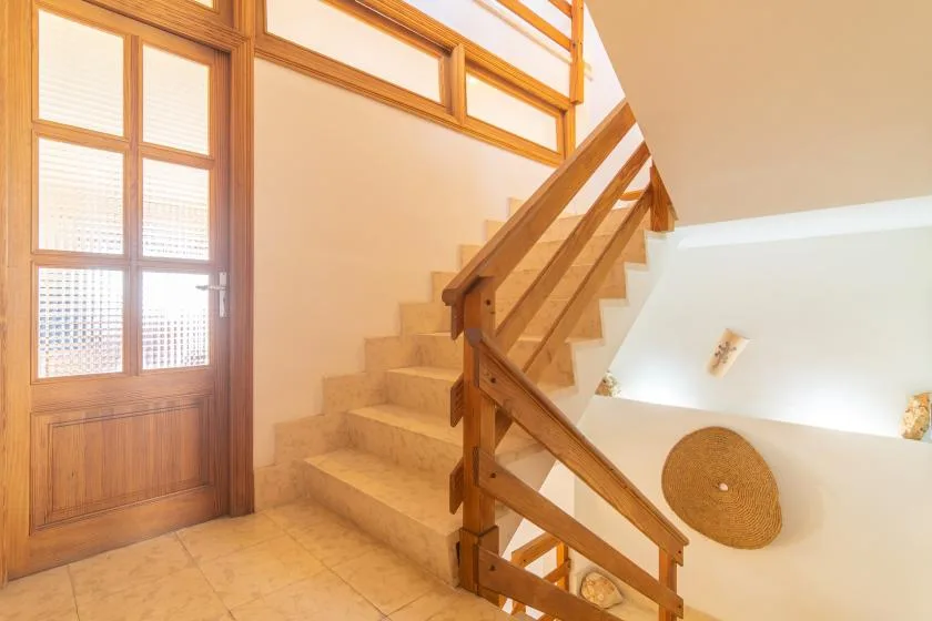 Una escalera con suelo de baldosas, barandillas de madera y una puerta acristalada.