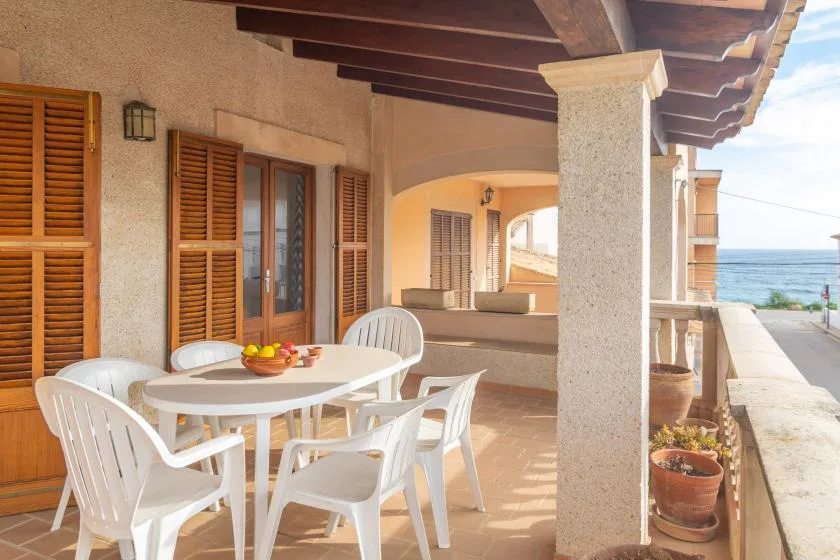 A covered seaside terrace has a dining table and white seating.