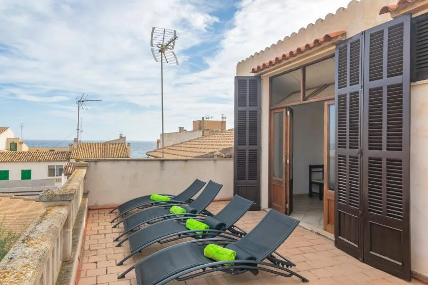 Una terraza en la azotea con asientos reclinables y una puerta abierta frente a tejados cercanos.