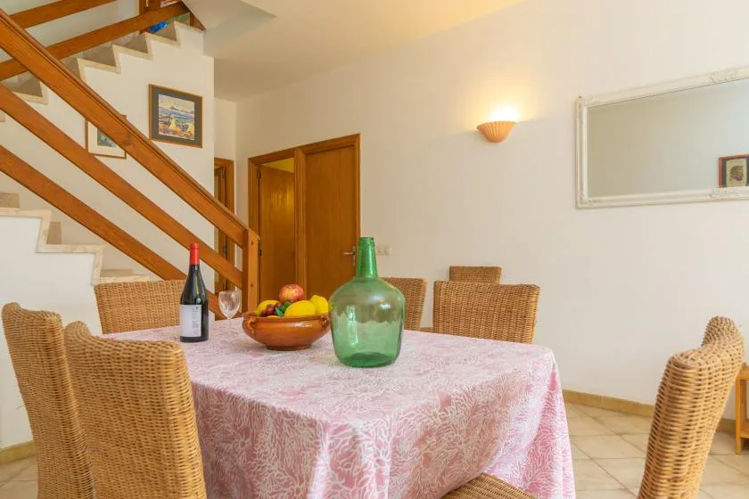 Un comedor con una mesa cubierta con un mantel rosa estampado y asientos de mimbre.