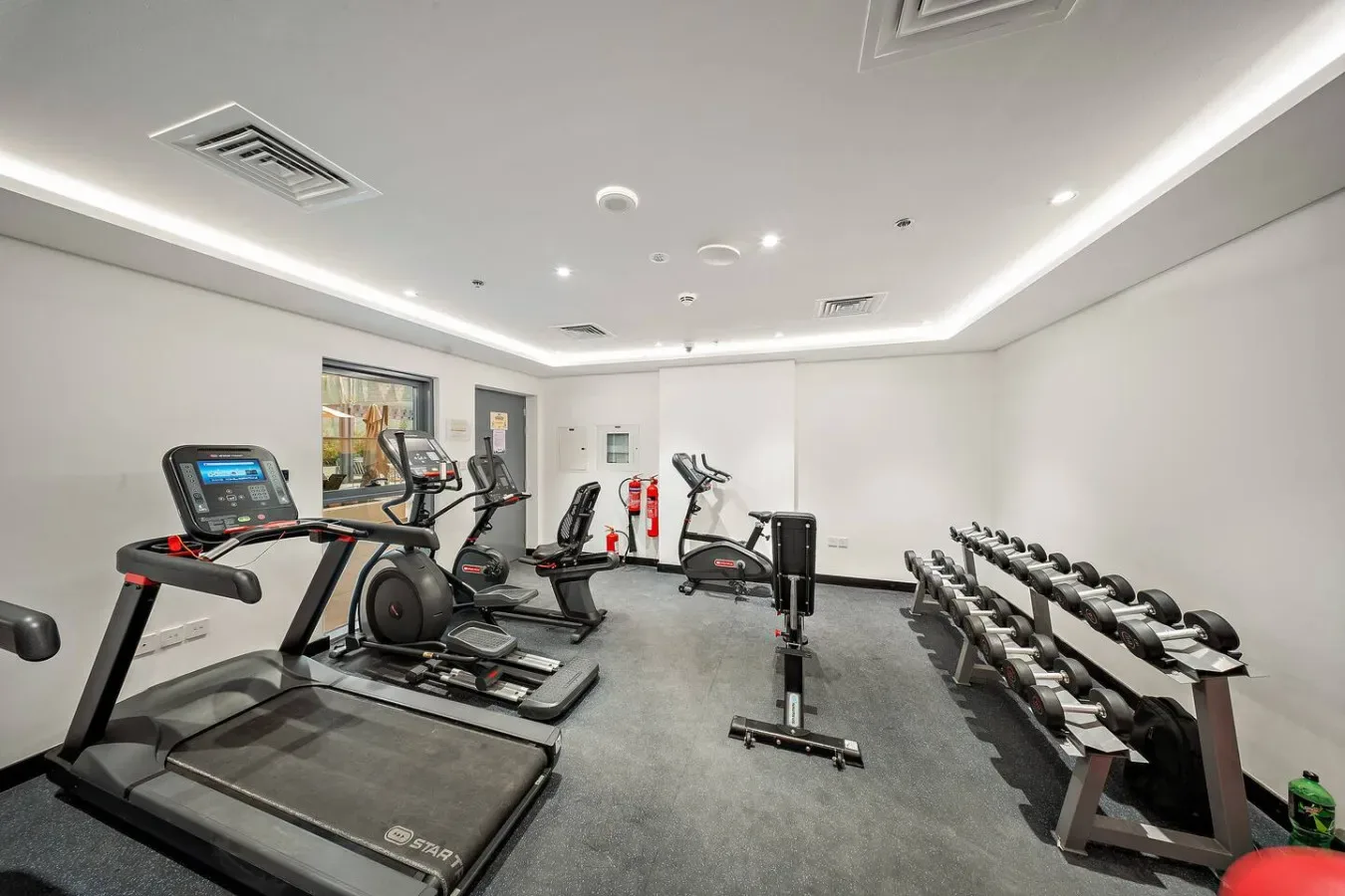 A gym with treadmills, exercise bikes, and a row of dumbbells.