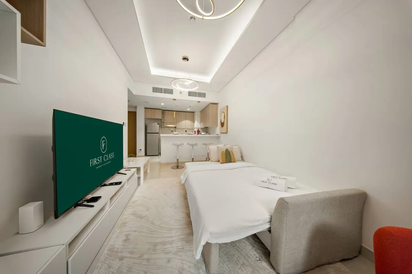 A bedroom with a bed facing a television and an open kitchenette behind it.