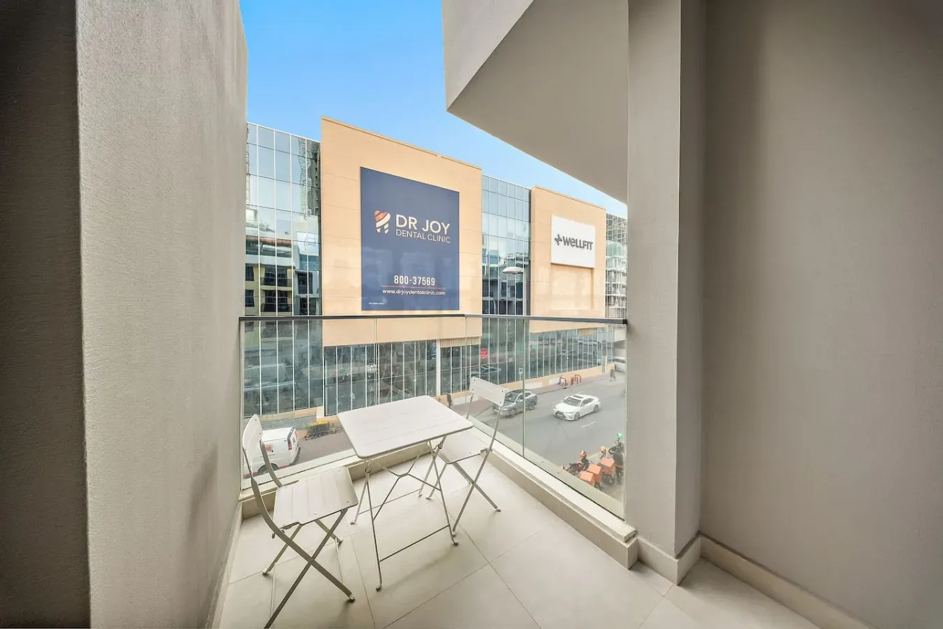 A balcony with a small table and seating overlooks a street of commercial buildings.