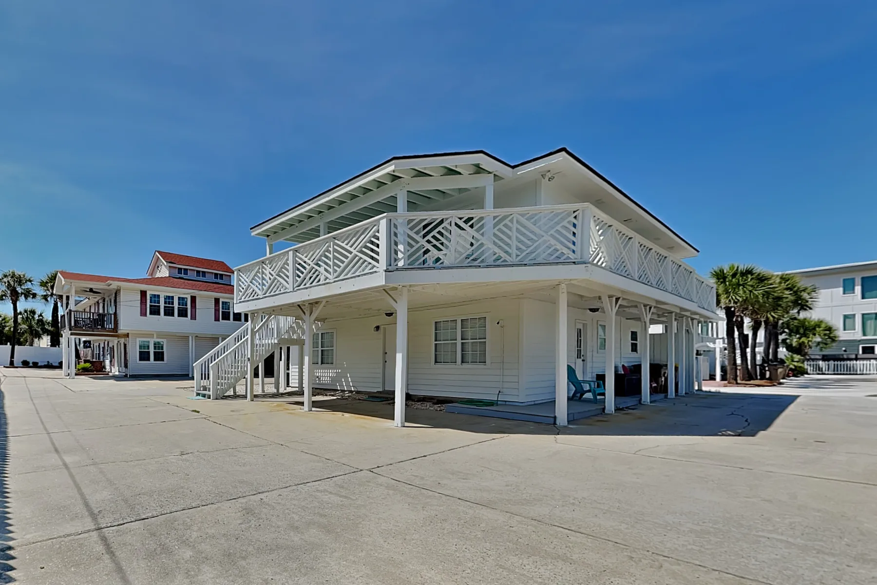 A raised coastal-style building with white railings stands beside a broad paved area.