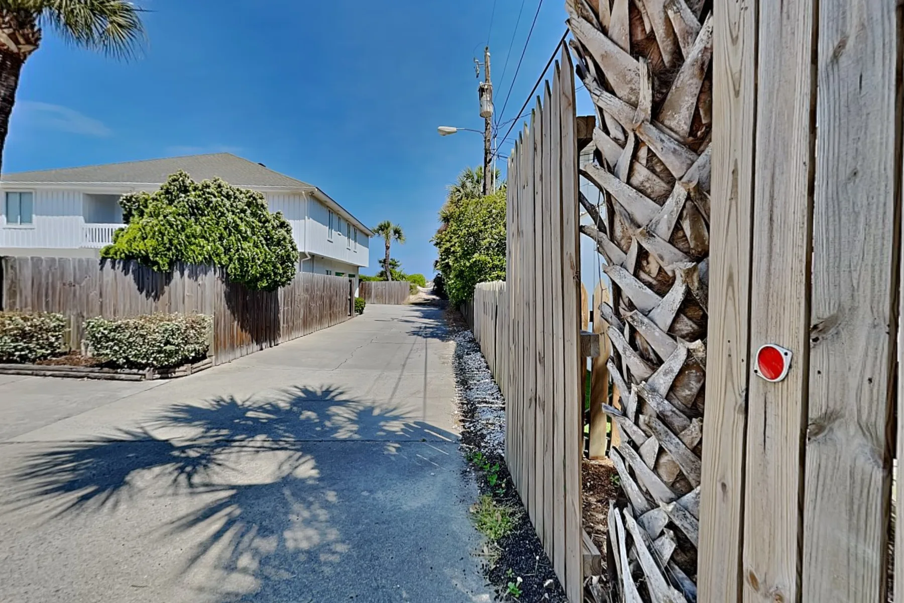 A paved lane runs between wooden fences and a white building under a clear sky.