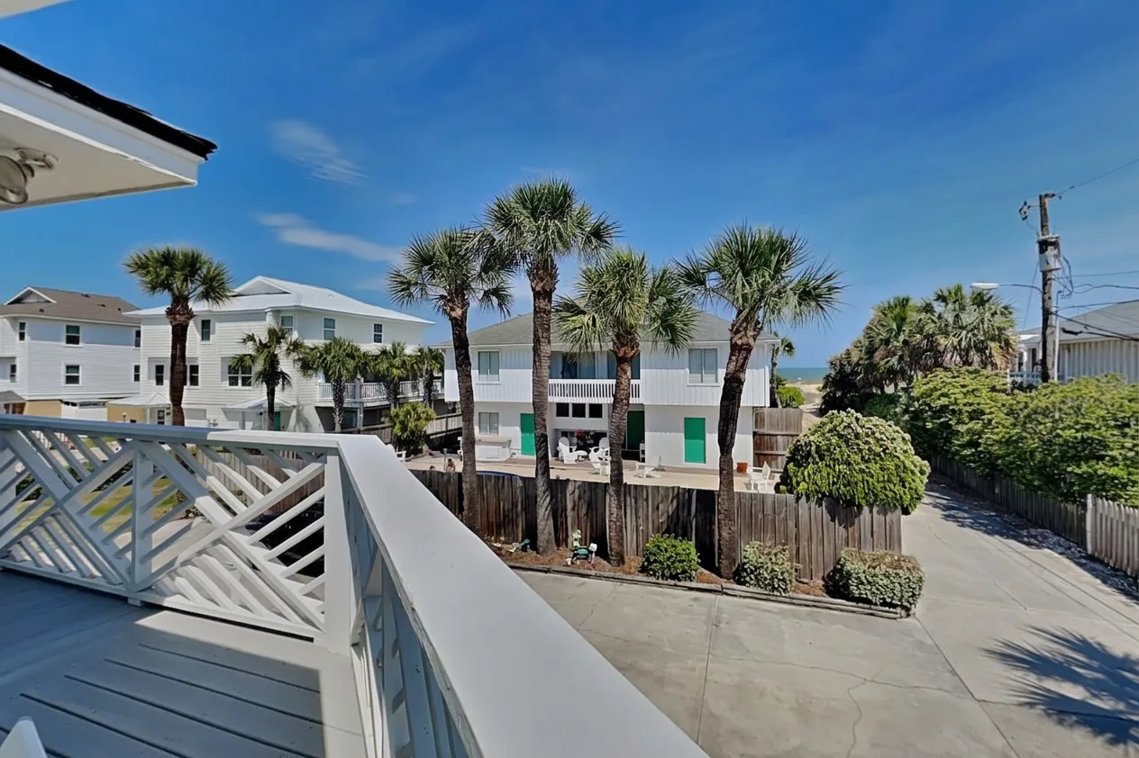 A balcony overlooks a sunny street lined with palm trees and low-rise buildings.
