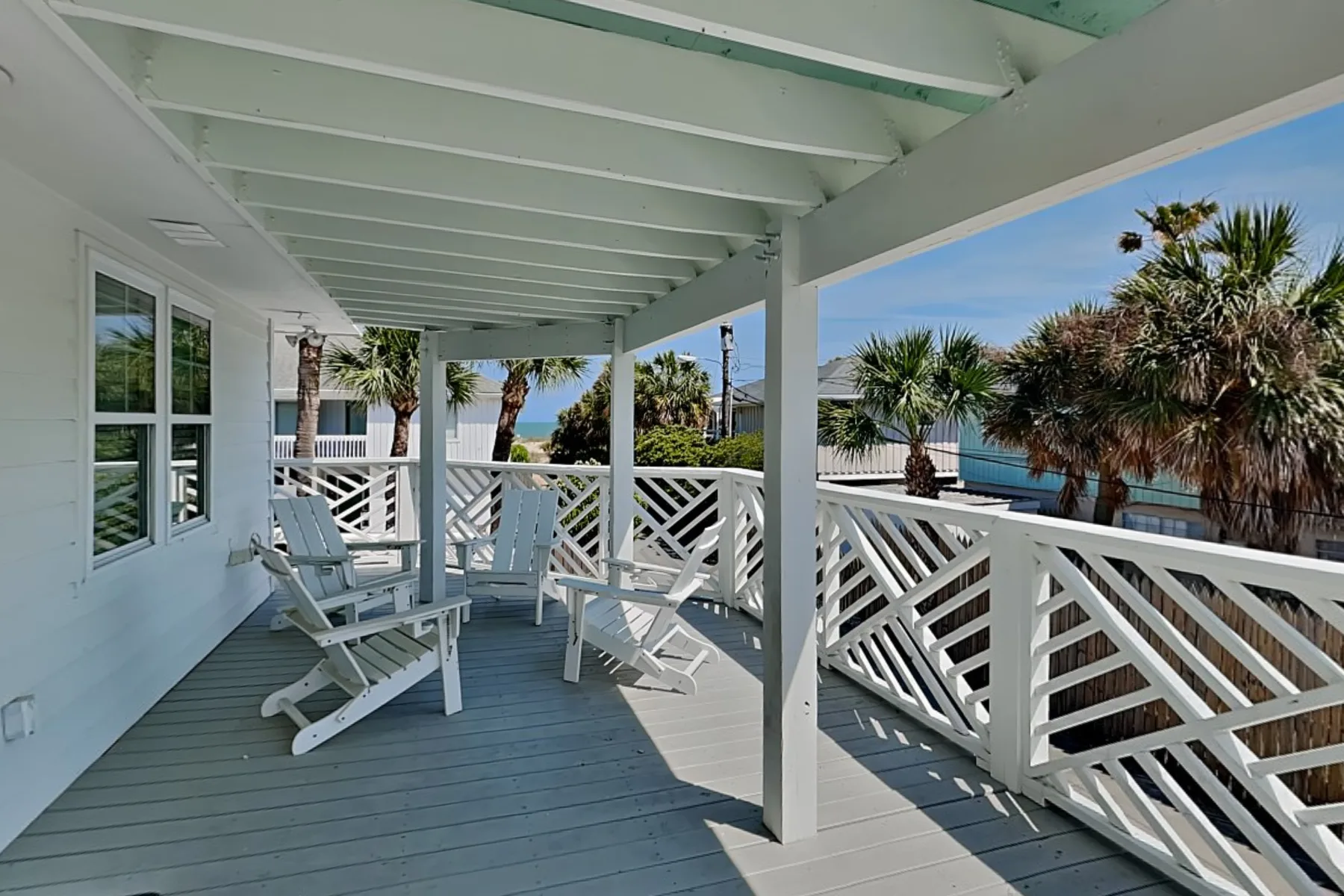 A covered outdoor deck with white railings and seating overlooks palm trees and water.