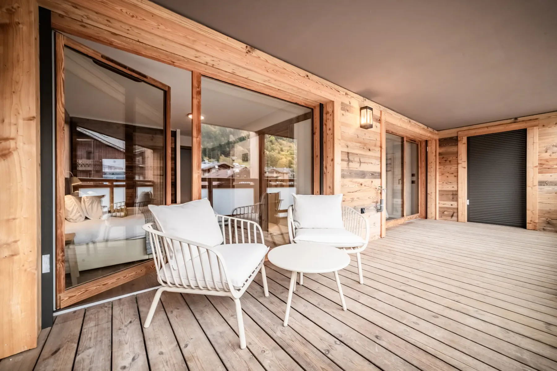 Two white chairs with cushions are placed on a wooden deck, with a wooden fence and a view of green hills and trees in the background.