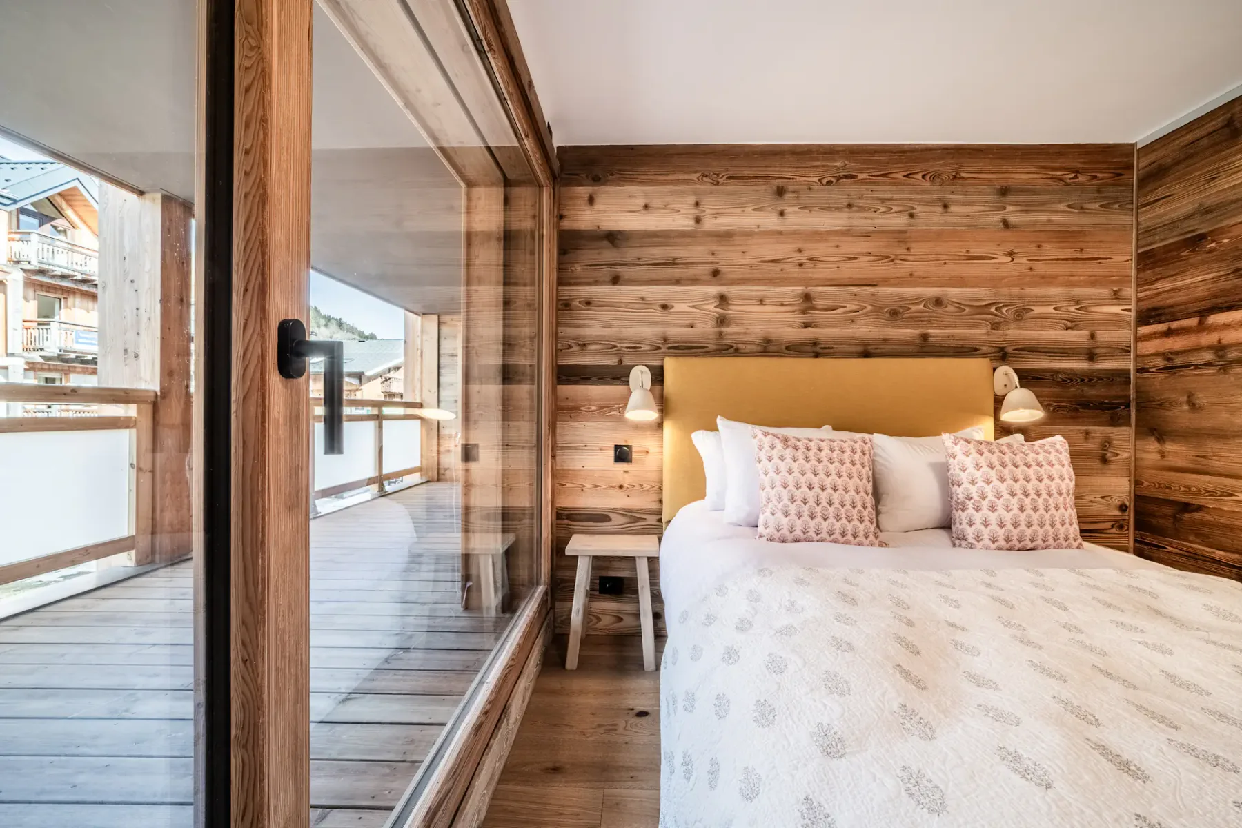 Cozy bedroom with a large bed, wooden walls, and a view of an outdoor balcony.