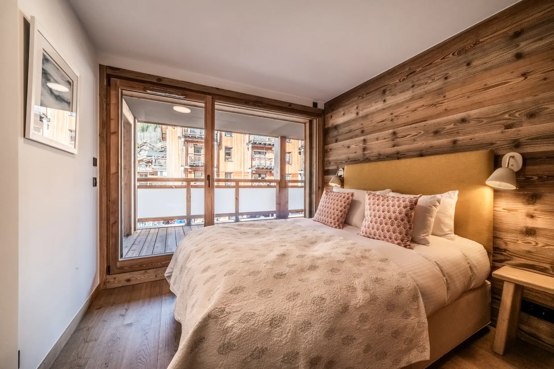 Cozy bedroom with a large bed, wooden walls, and a view of an outdoor balcony.