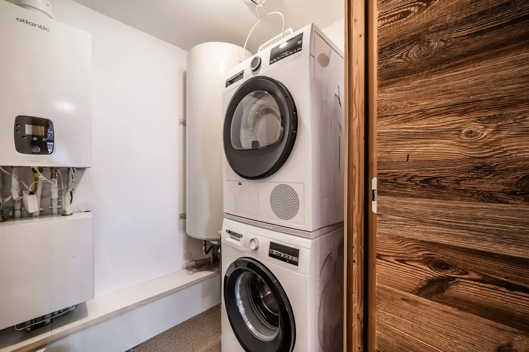 A stacked washer and dryer in a utility room with a wooden door and white walls.