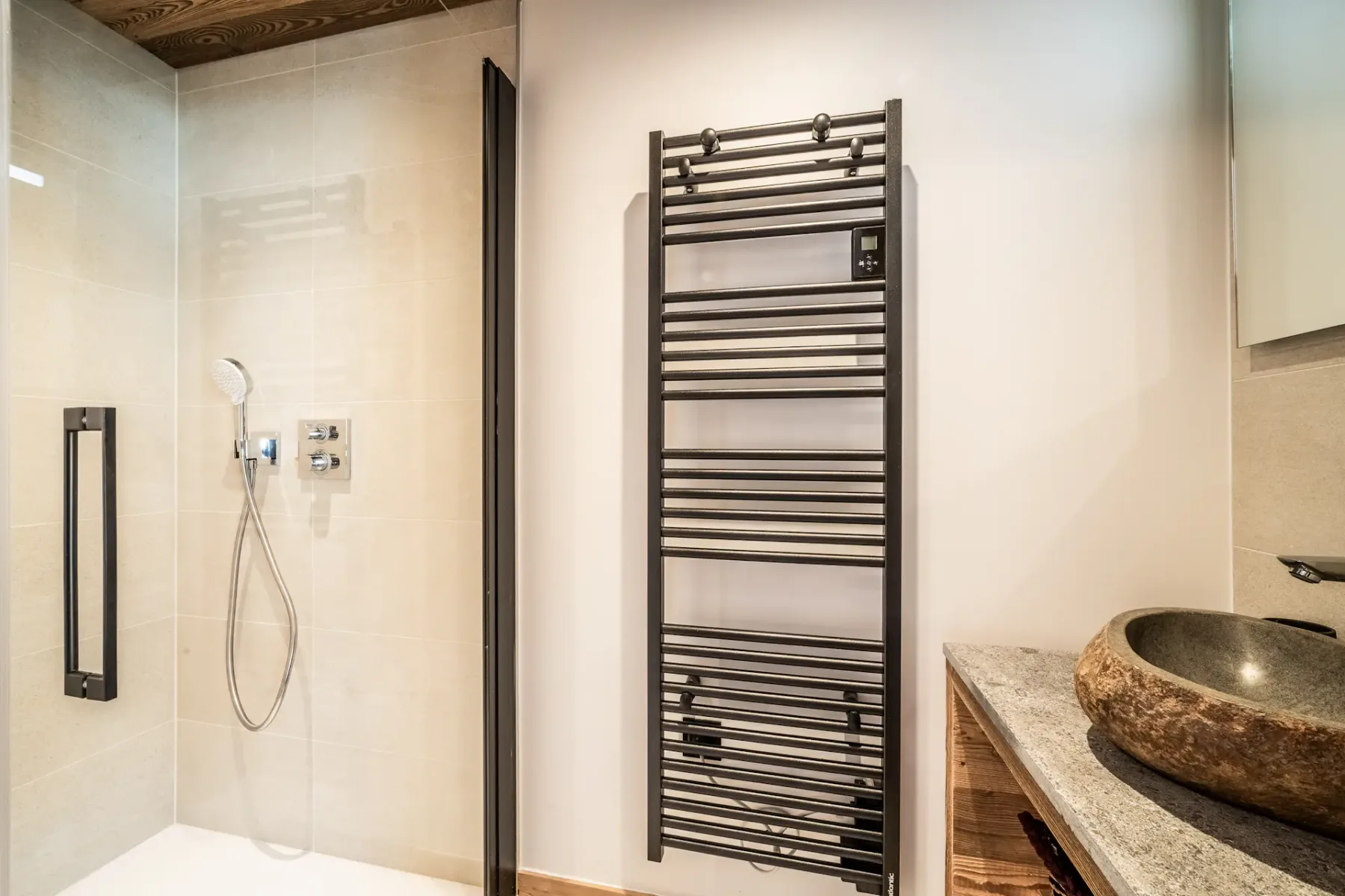 Modern bathroom featuring a walk-in shower, black vertical towel radiator, and a stone sink on a wooden countertop.