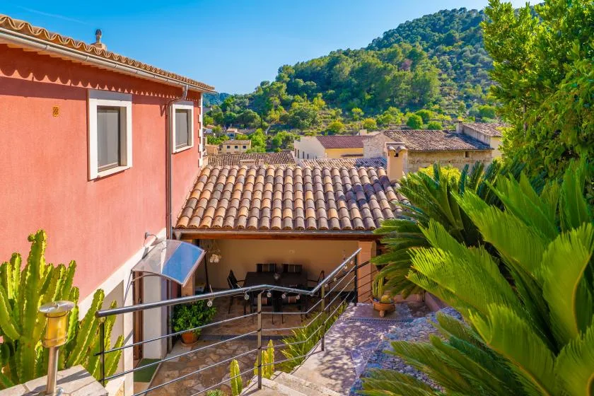A tiled-roof patio sits beside a coral-colored building, with green hills in the background.