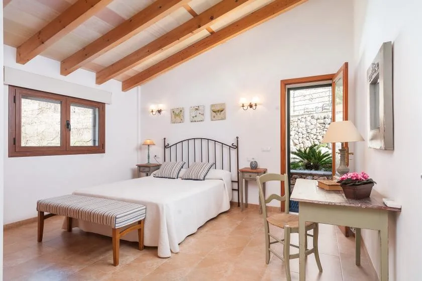 A bright bedroom with a double bed, exposed wooden ceiling beams, and a small desk.