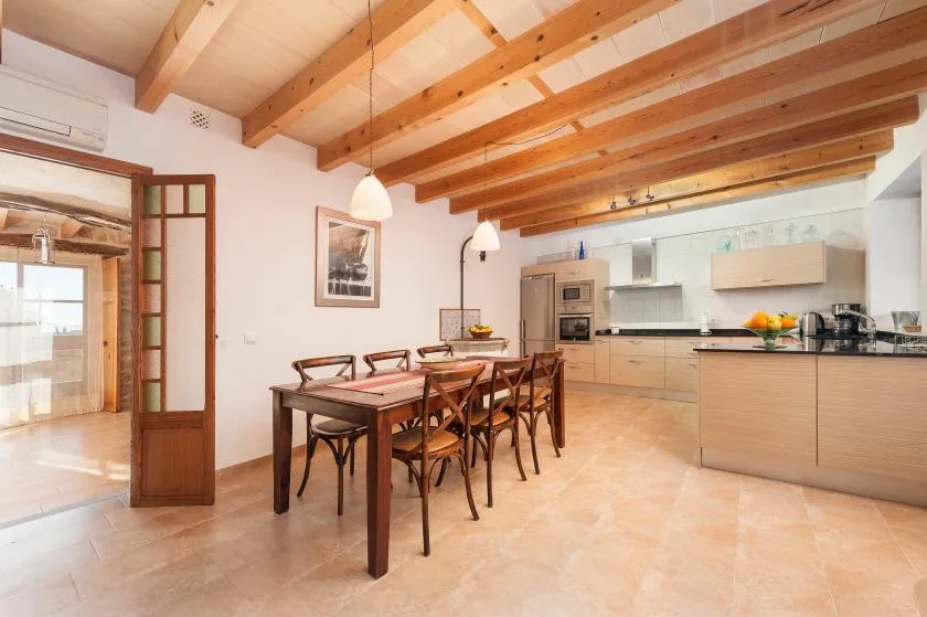 An open-plan kitchen and dining area with a wooden table beneath exposed beams.