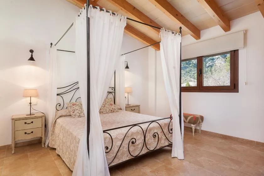 A bedroom with a wrought-iron canopy bed and a window overlooking greenery.