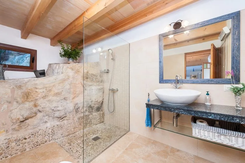 A bathroom with a glass shower, stone wall, and sink beneath a large mirror.