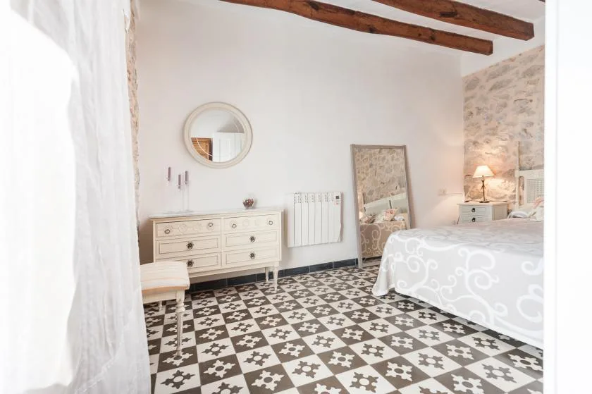 A bright bedroom with patterned tile flooring and a bed beside a stone wall.