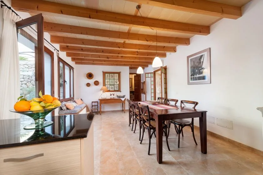 A dining room with a long table and chairs beneath exposed wooden ceiling beams.
