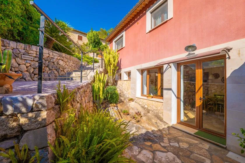 A sunlit stone patio runs alongside a pink house with glass doors.